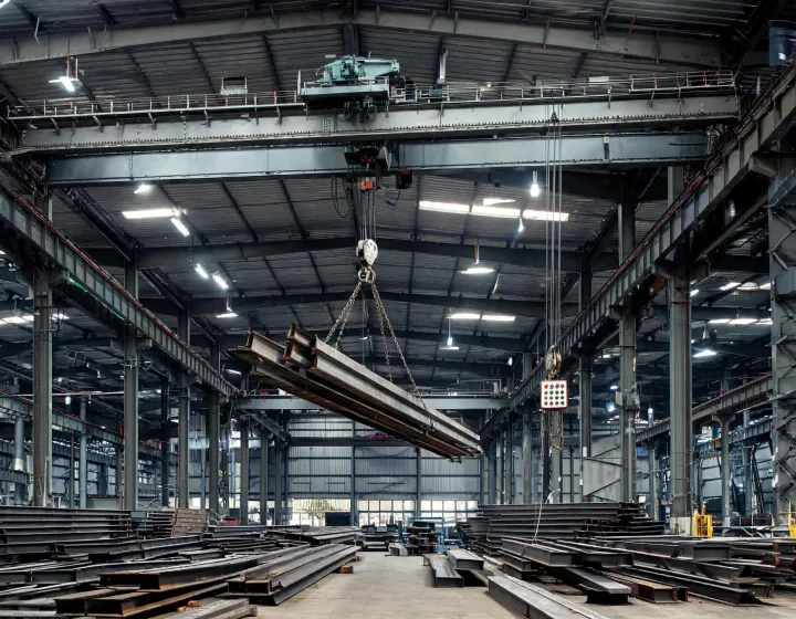 Demag overhead crane lifting steel girders inside fabrication bay
